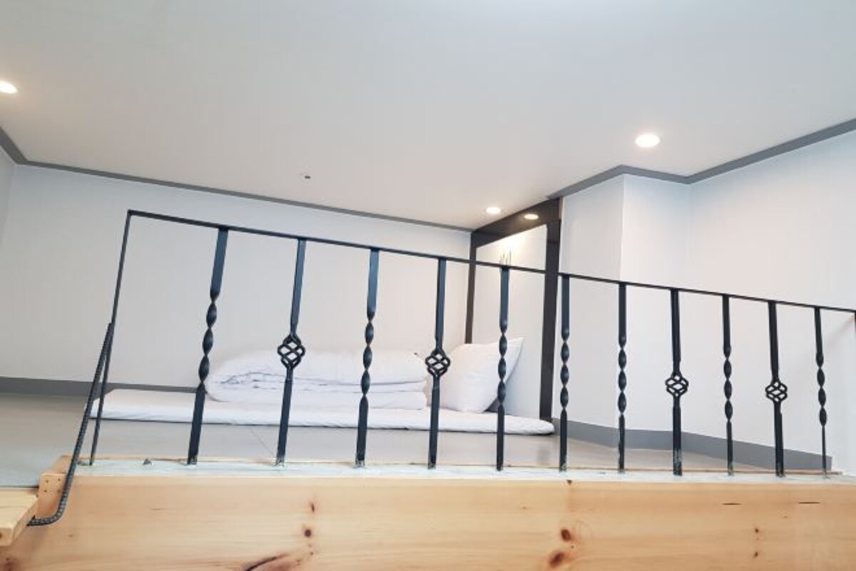 A wooden staircase with a metal railing leading to a white room with a bed and a nightstand.