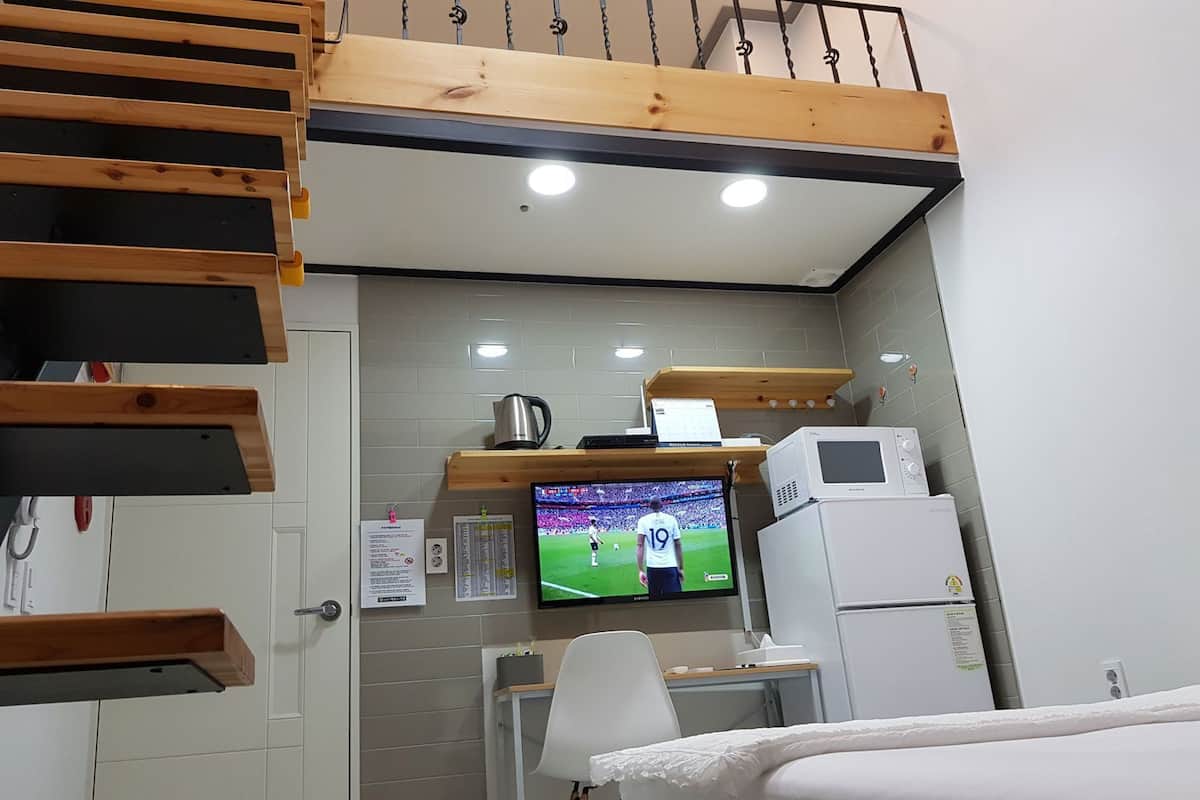 Habitación compacta con una cama litera, un escritorio con computadora, televisión y refrigerador.