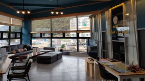 Een moderne hotelkamer met een groot raam, een houten plafond en een zithoek met een bank en stoelen.