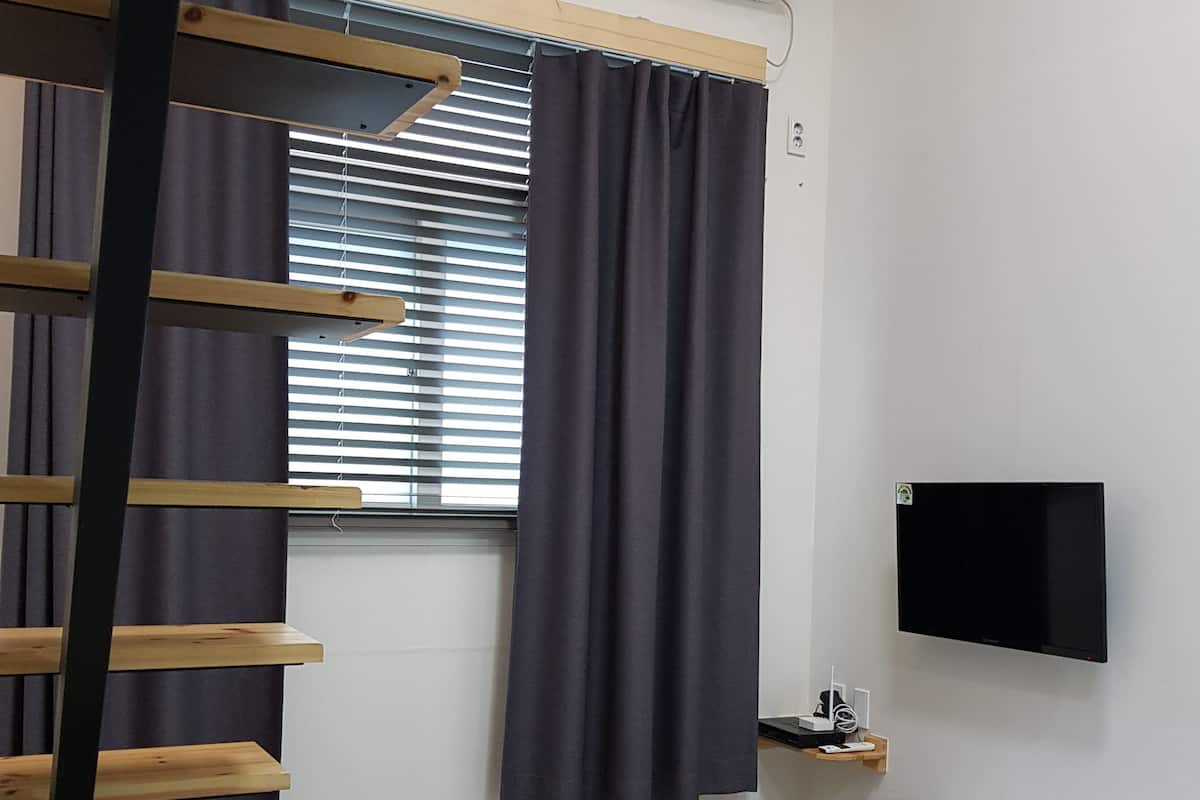 Un dormitorio con literas, un escritorio, un televisor de pantalla plana y una ventana con persianas y cortinas.