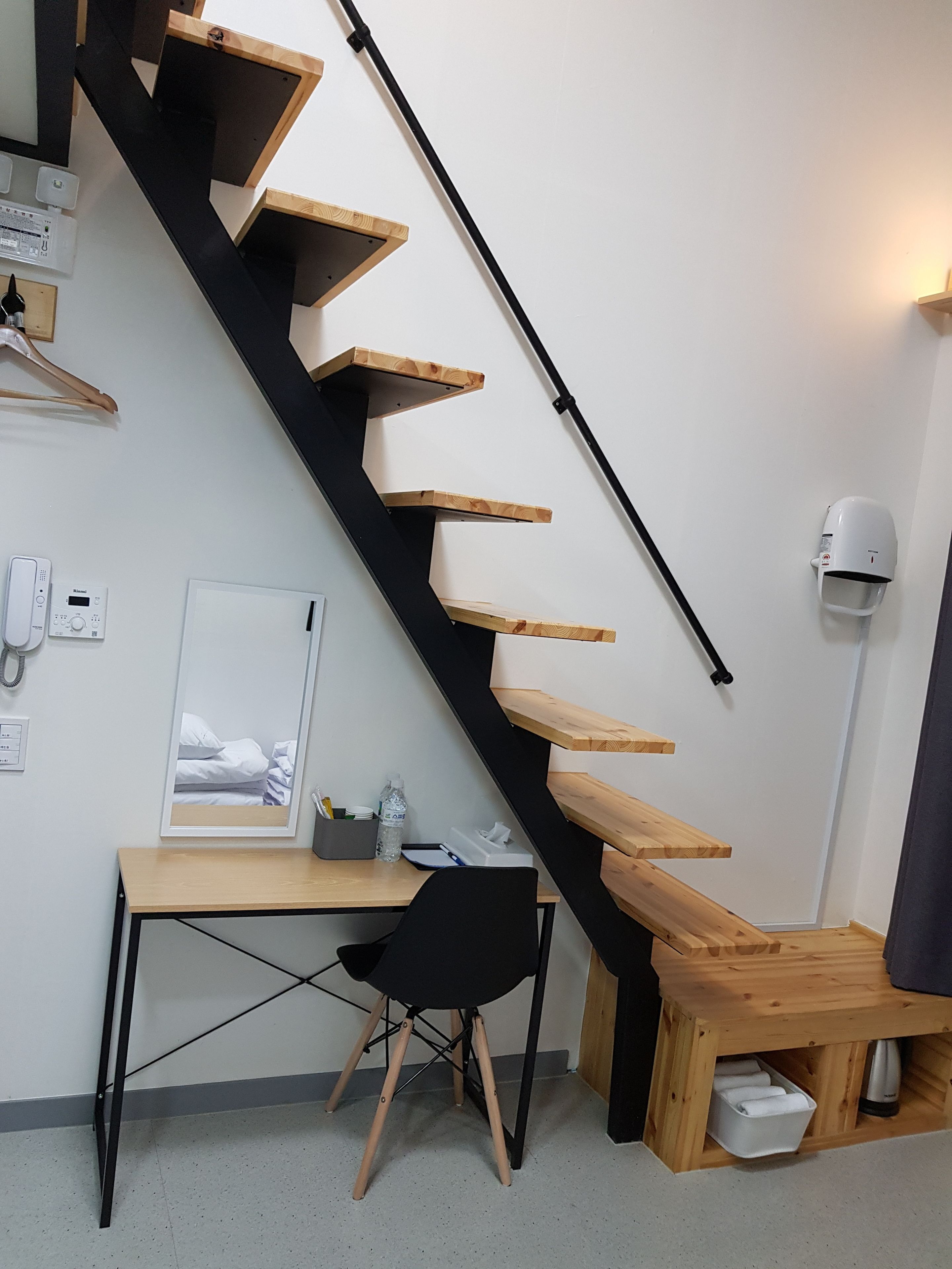 A modern room with a black staircase, wooden desk, and a black chair.