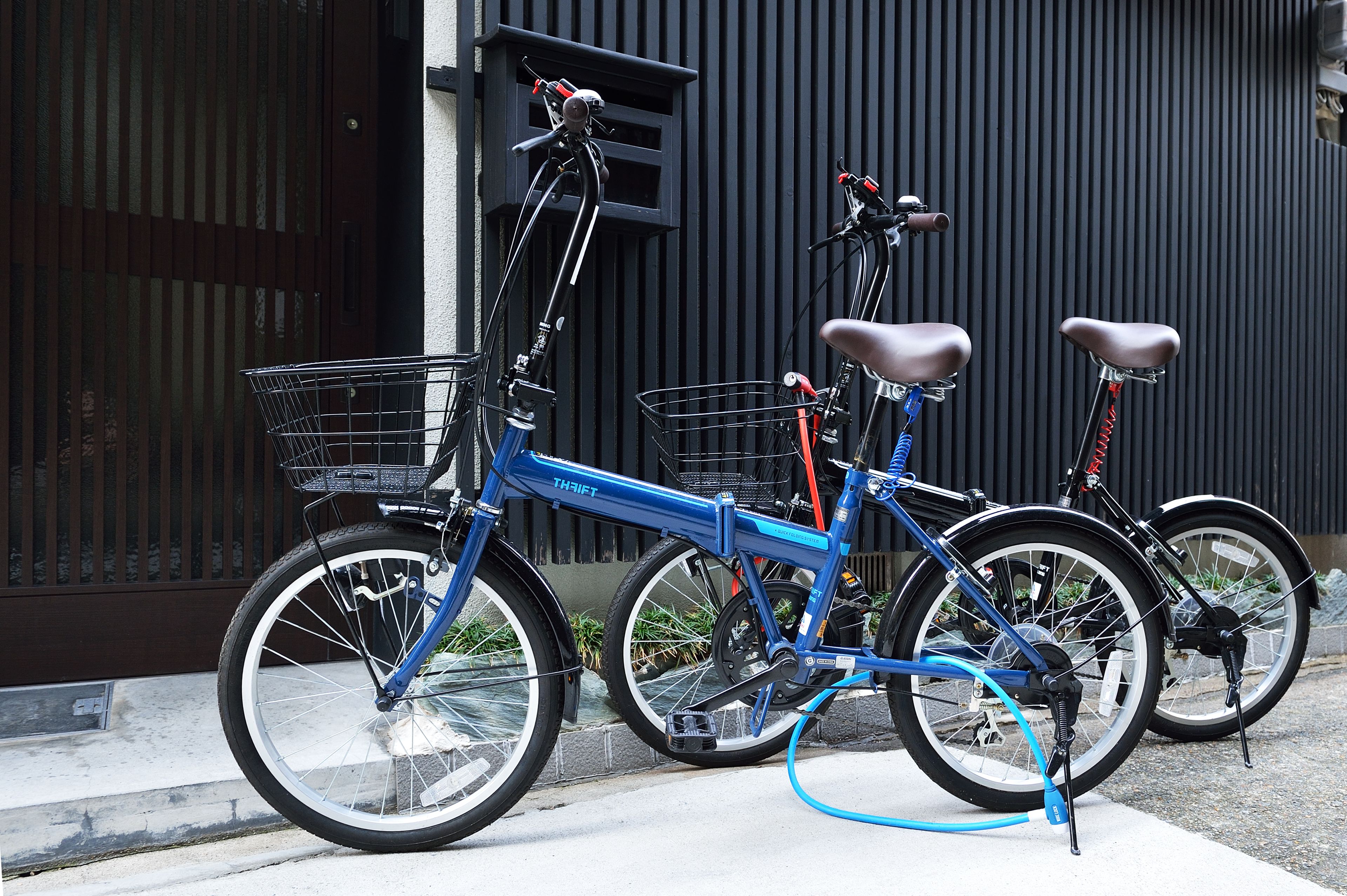 Een blauwe fiets met een mandje en een ketting, geparkeerd tegen een donker gebouw.