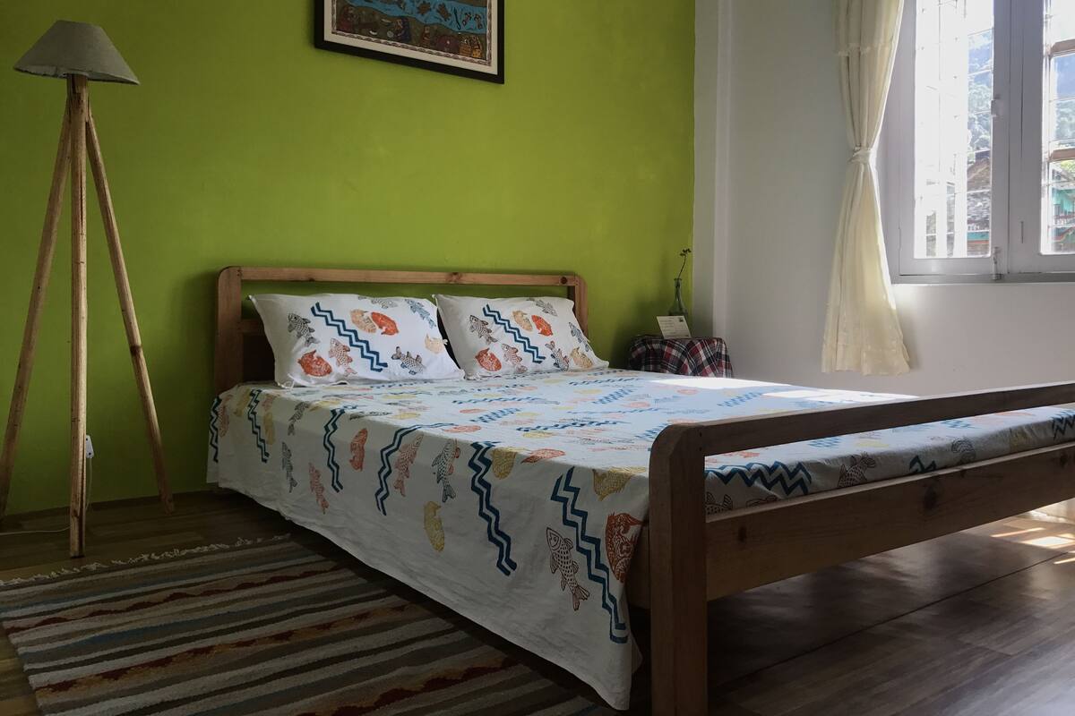 A room with a bed, a standing lamp, a framed picture on the wall, and a window with curtains.