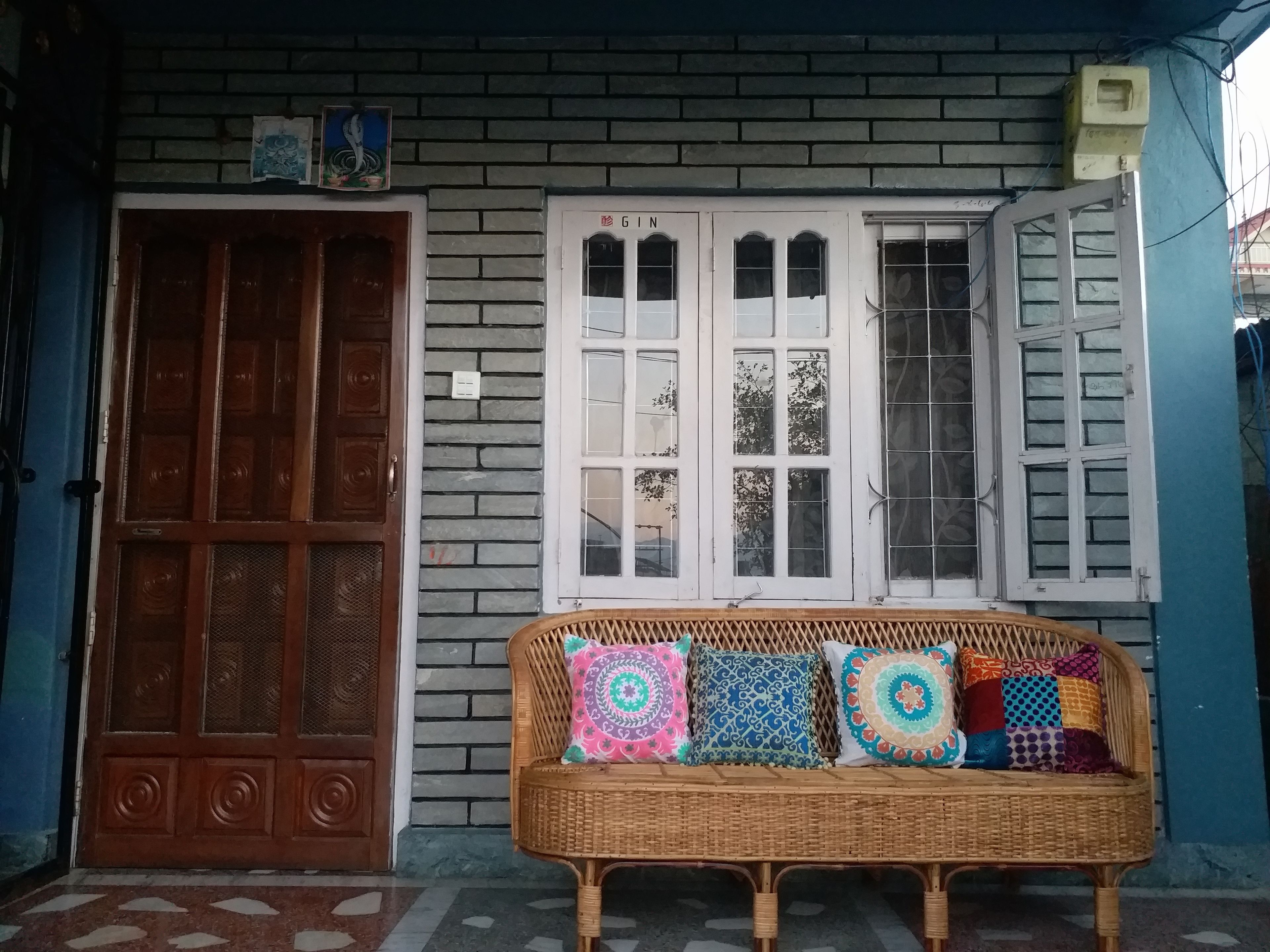 A wicker sofa with colorful cushions in front of a building with a brick facade and white-framed windows.