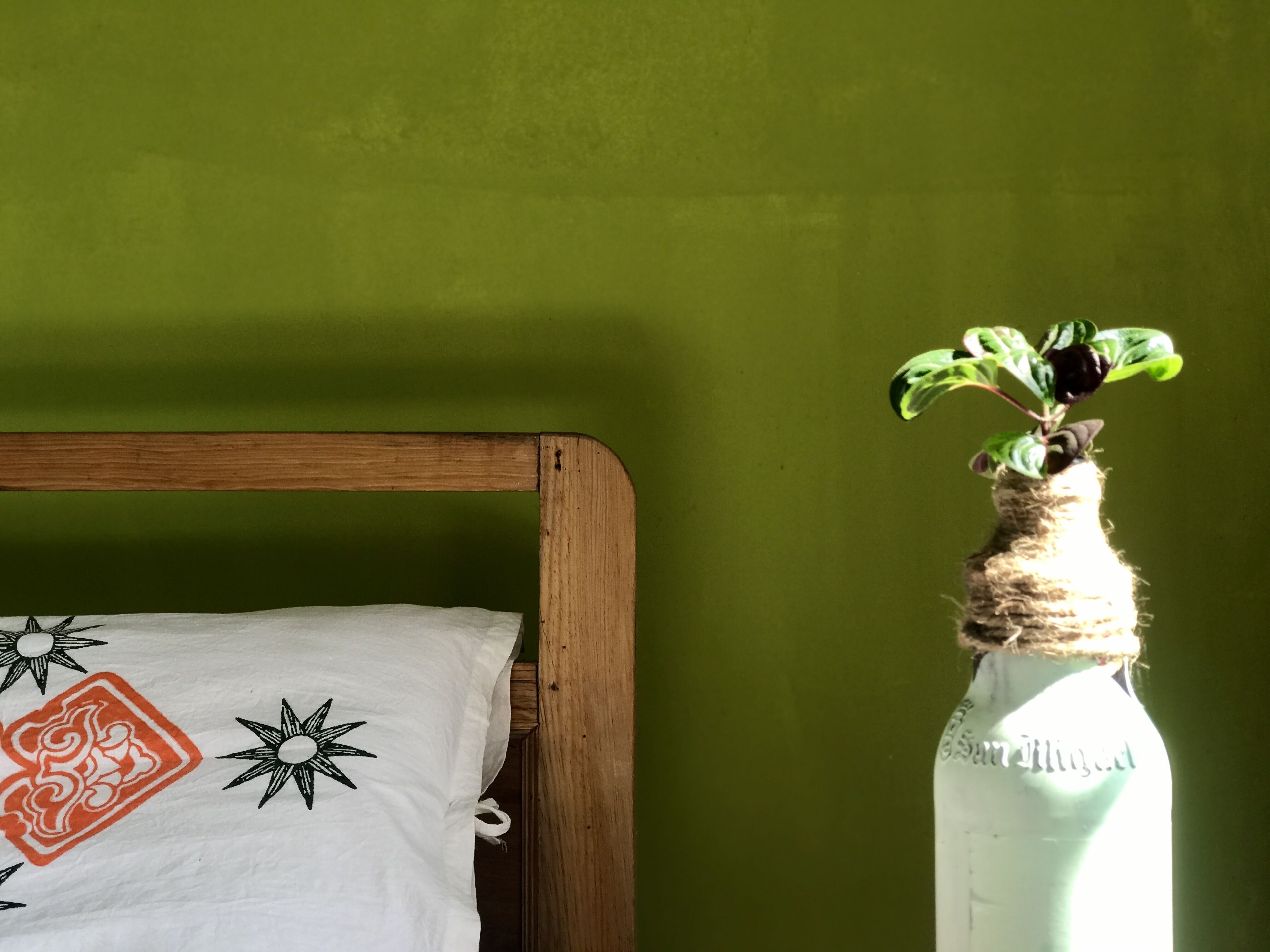 A bed with a white pillow featuring black and orange designs, a wooden headboard, and a green wall in the background.