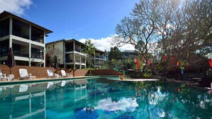 A swimming pool with clear blue water, surrounded by lounge chairs and a building with balconies. - Bansaeo Garden and Resort (Chiang Saen)