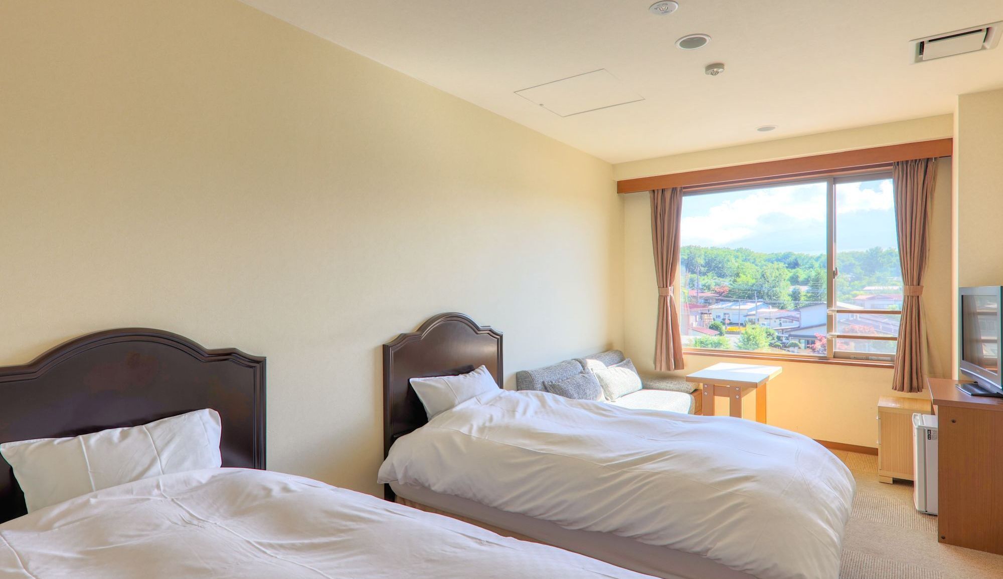 Een hotelkamer met twee bedden, een klein tafeltje, een televisie en een raam met uitzicht op een stadsbeeld.