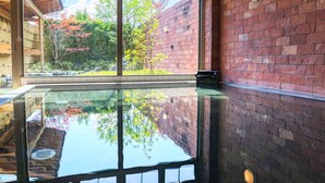 A room with a large glass window reflecting a garden with trees and a brick wall. - Fujimatsuzono Hotel (Yamanakako)