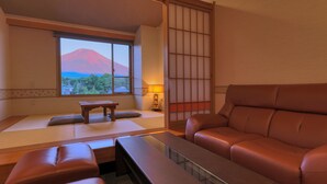 A traditional Japanese room with tatami flooring, a low table, a cushioned bench, and a view of a mountain. - Fujimatsuzono Hotel (Yamanakako)