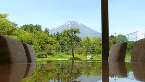A view of Mount Fuji reflected in a calm body of water, with lush greenery and a wooden fence in the foreground. - Fujimatsuzono Hotel (Yamanakako)