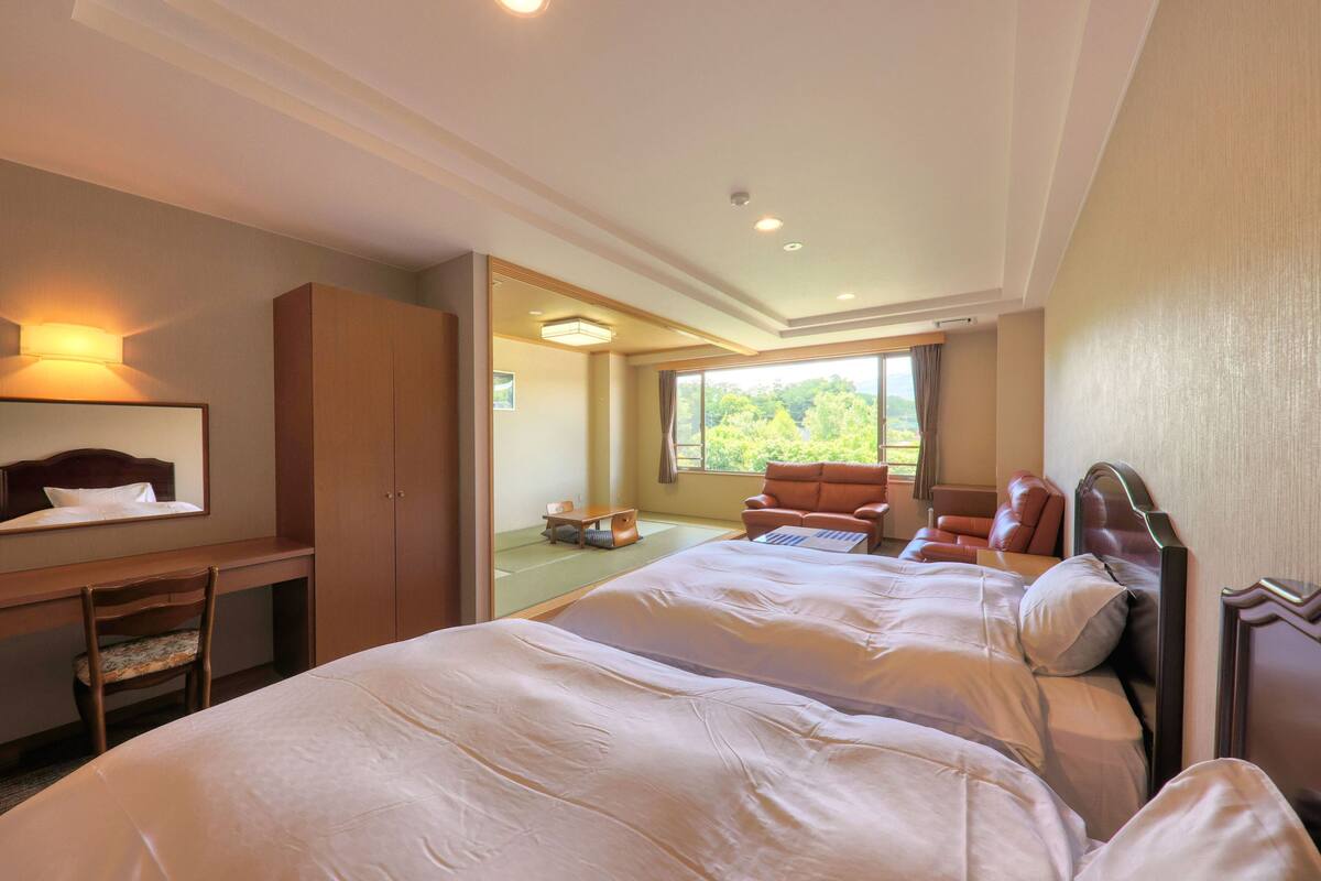 Une chambre d’hôtel avec deux lits, un bureau, une chaise et une vue sur l’extérieur.