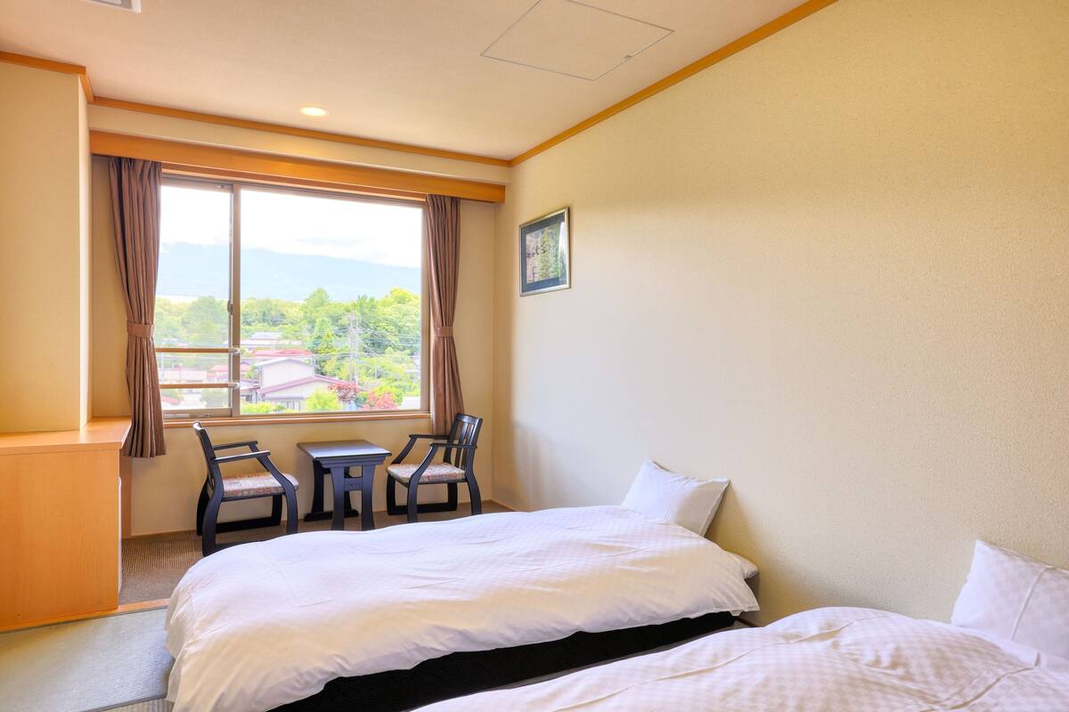 Une chambre d’hôtel avec un lit, deux chaises, une petite table et une fenêtre avec des rideaux.
