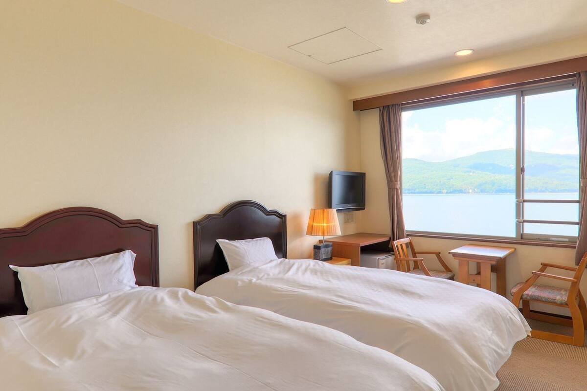 Une chambre d’hôtel avec deux lits, un bureau avec une lampe, une télévision et une vue sur un lac.