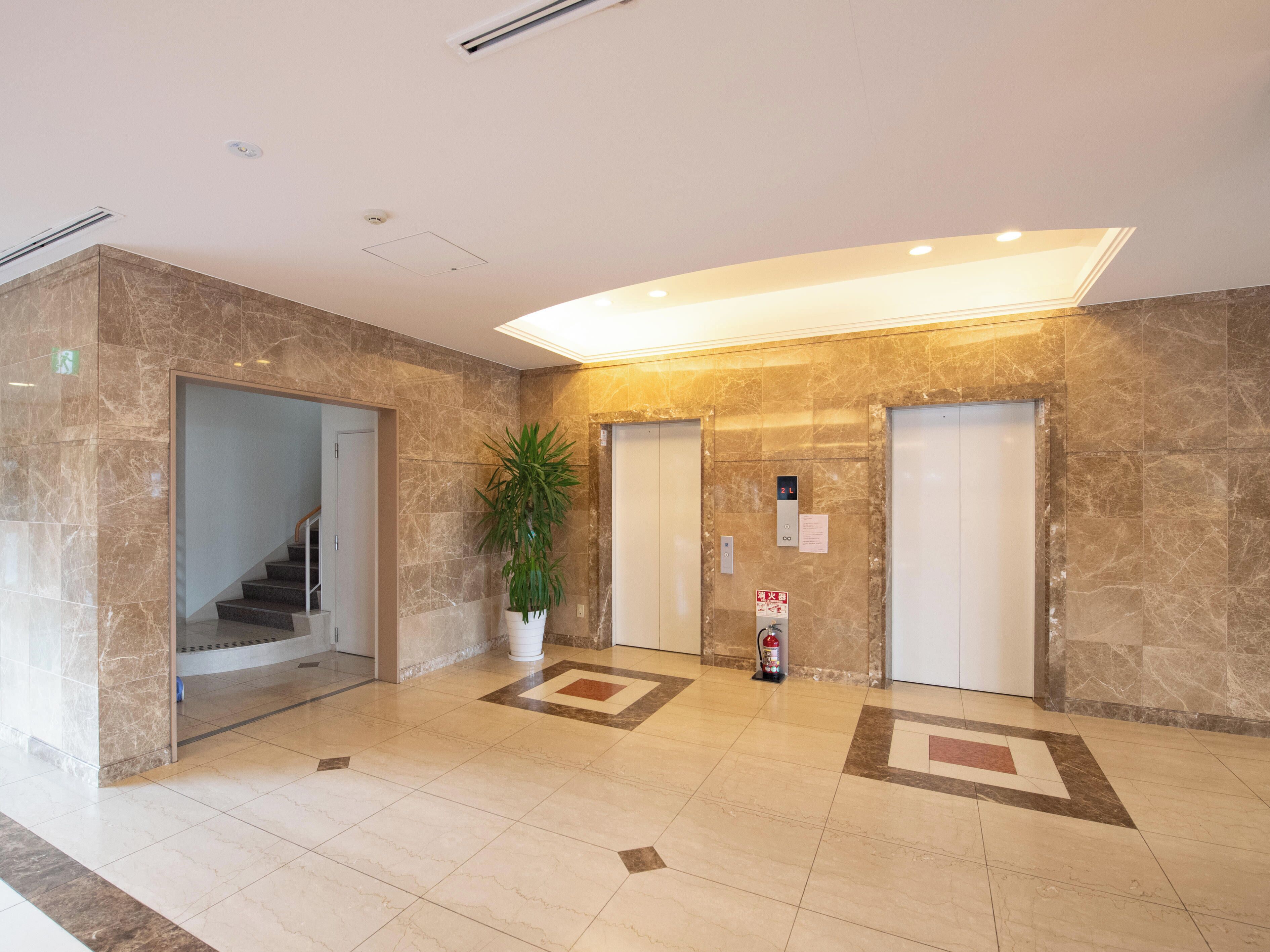 A lobby with marble flooring, a potted plant, two elevators, and a staircase.