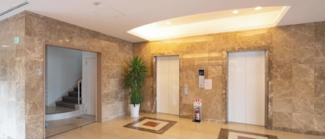 A lobby with marble flooring, a potted plant, two elevators, and a staircase.