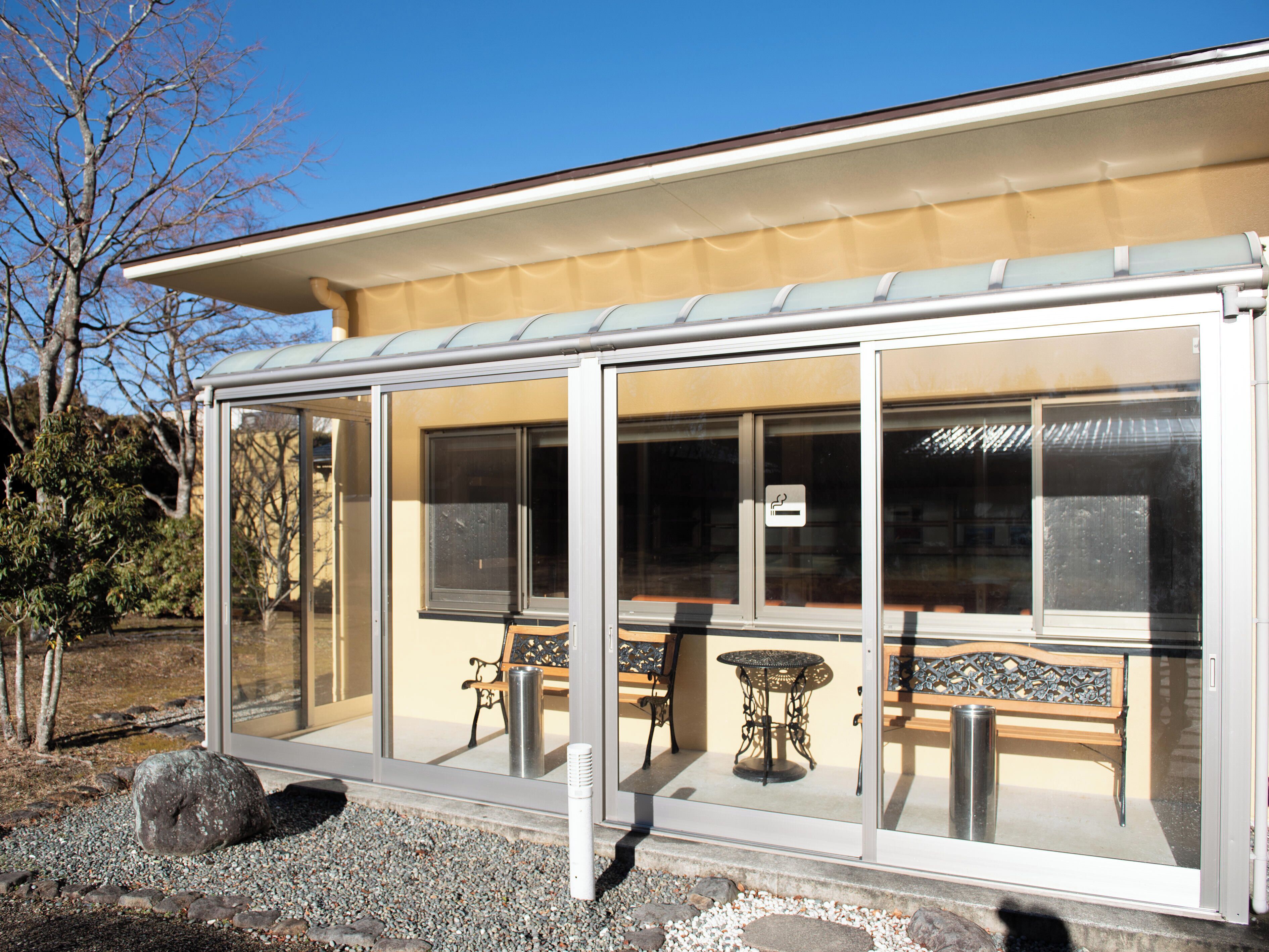 A covered outdoor seating area with a table and benches, a trash can, and a clear glass enclosure.