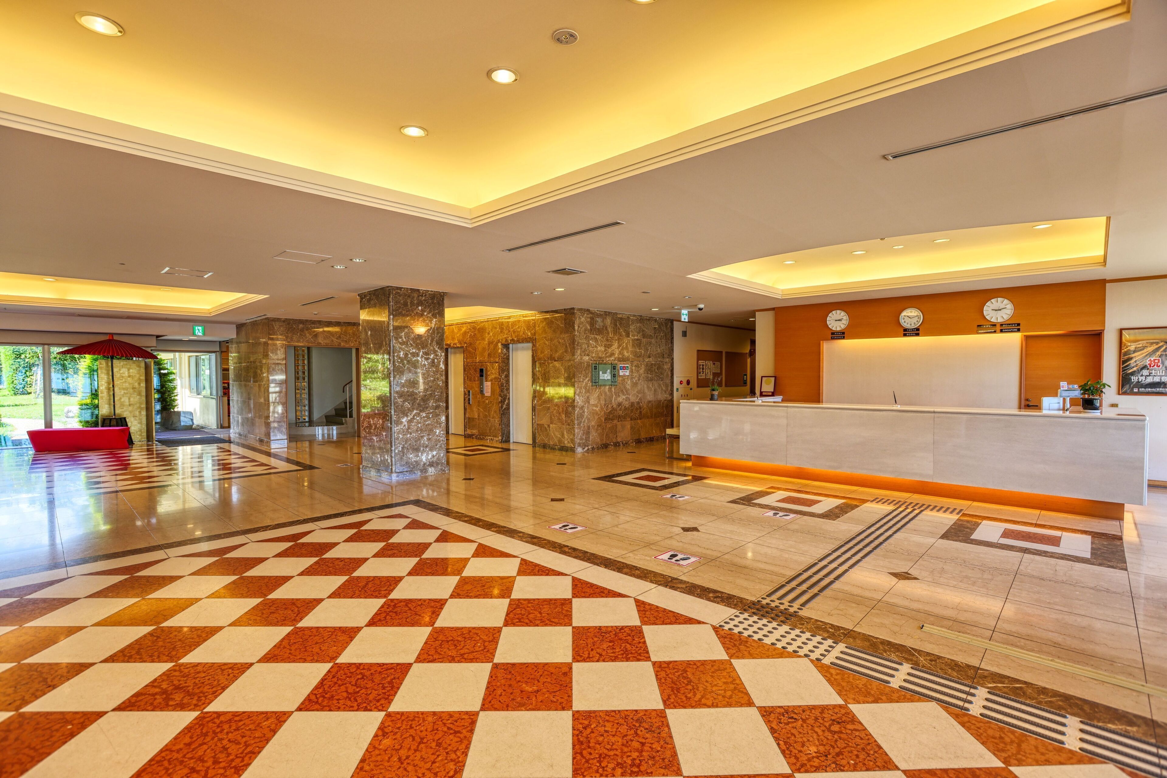 A hotel lobby with a checkered floor, a reception desk, and a red seating area.