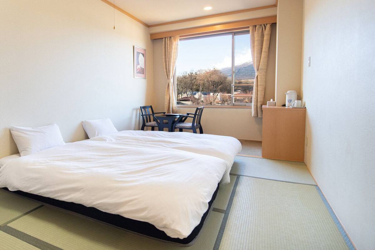 Une chambre d’hôtel avec un lit, une chaise, une petite table et une fenêtre donnant sur l’extérieur.