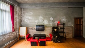 A room with a wooden floor, red chairs, a black bear statue, a TV on the wall, and a red curtain. - Farmland B&B (Sanxing)