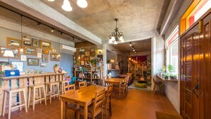 A spacious dining area with wooden tables and chairs, a bar area with stools, and a variety of framed pictures on the walls. - Farmland B&B (Sanxing)