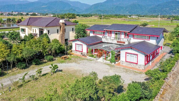 A large, multi-story house with a covered patio area, surrounded by lush greenery and mountains in the background. - Farmland B&B (Sanxing)