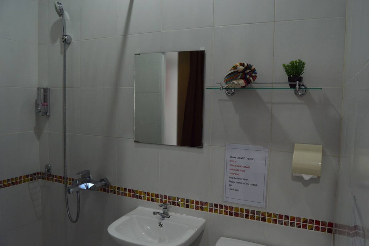 Casa de banho com chuveiro, lavatório e espelho. Há um aviso na parede com instruções.
