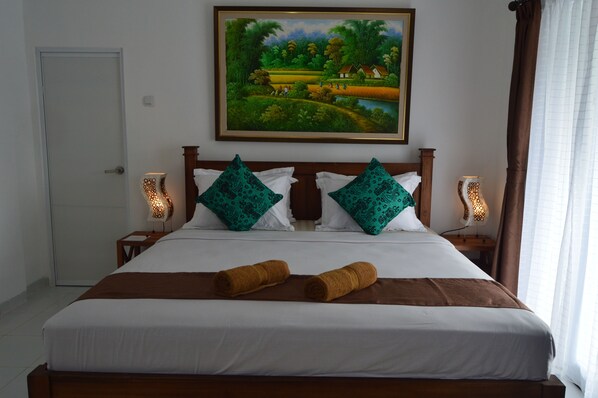 A neatly made bed with a brown headboard, two decorative pillows, and two rolled towels. - Askara Guest House - Hostel (Ubud)