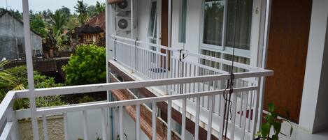 Un immeuble à plusieurs étages, doté d’un balcon avec une rambarde blanche, d’un pot de fleurs et d’une porte en bois.