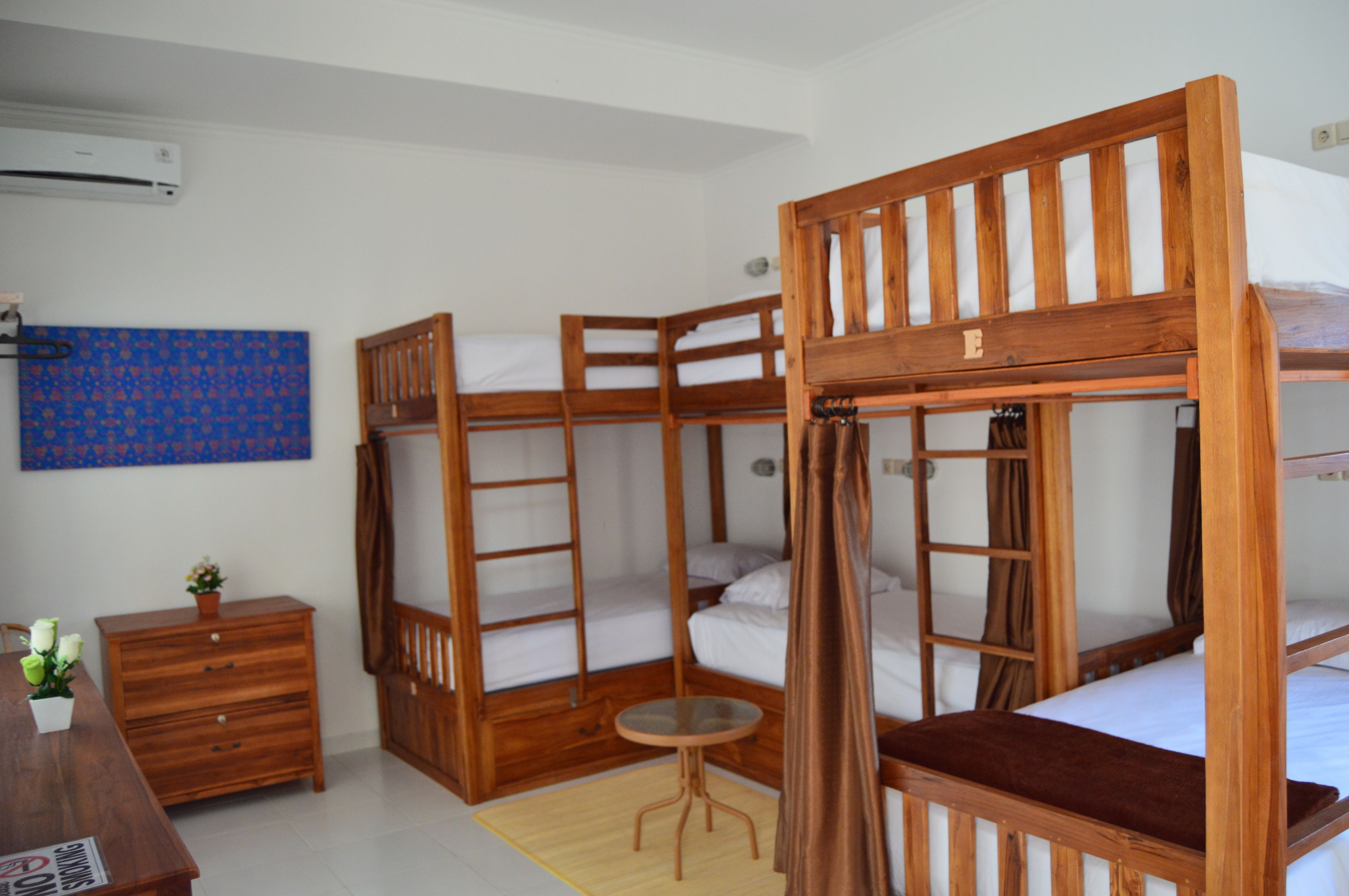 Quarto com beliches, uma pequena mesa de madeira, cômoda e parede com padrão azul.