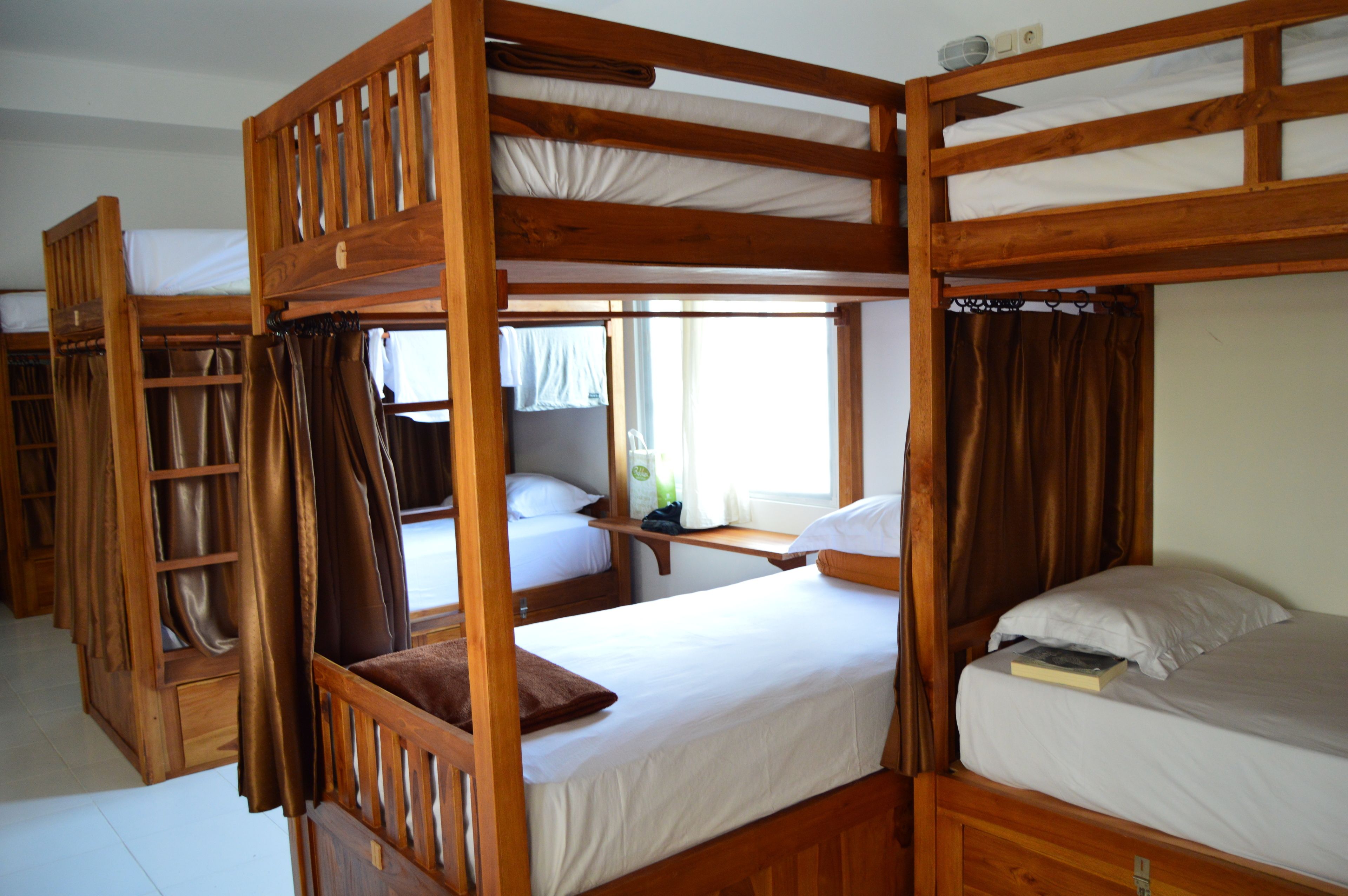 A dormitory-style room with bunk beds, a small table, and a window with curtains.