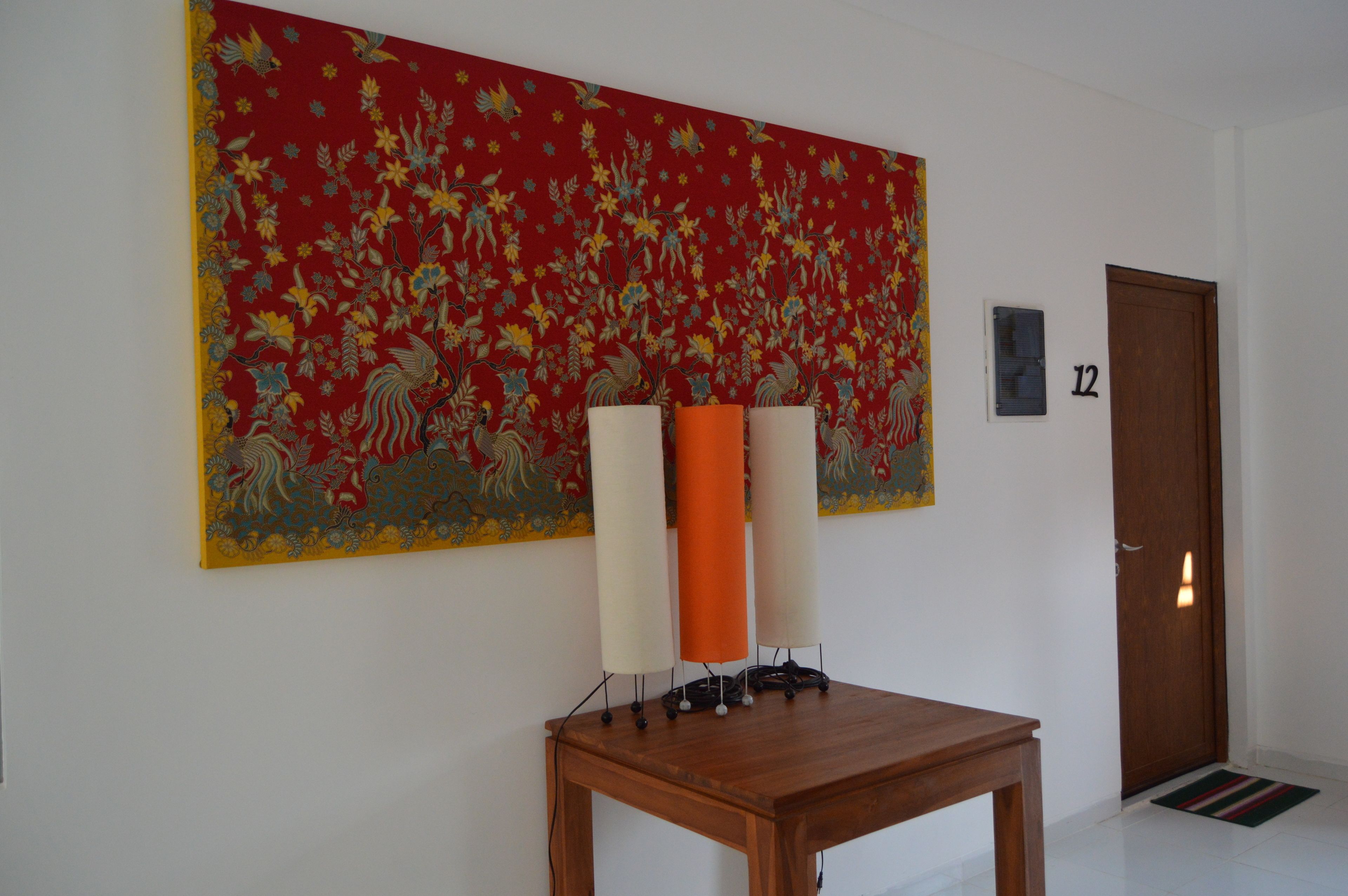 A room with a large floral tapestry, a wooden table with three candles, and a door marked with the number 12.