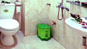 Une salle de bain avec des toilettes, une poubelle verte, une douche et un lavabo décoré de fleurs.