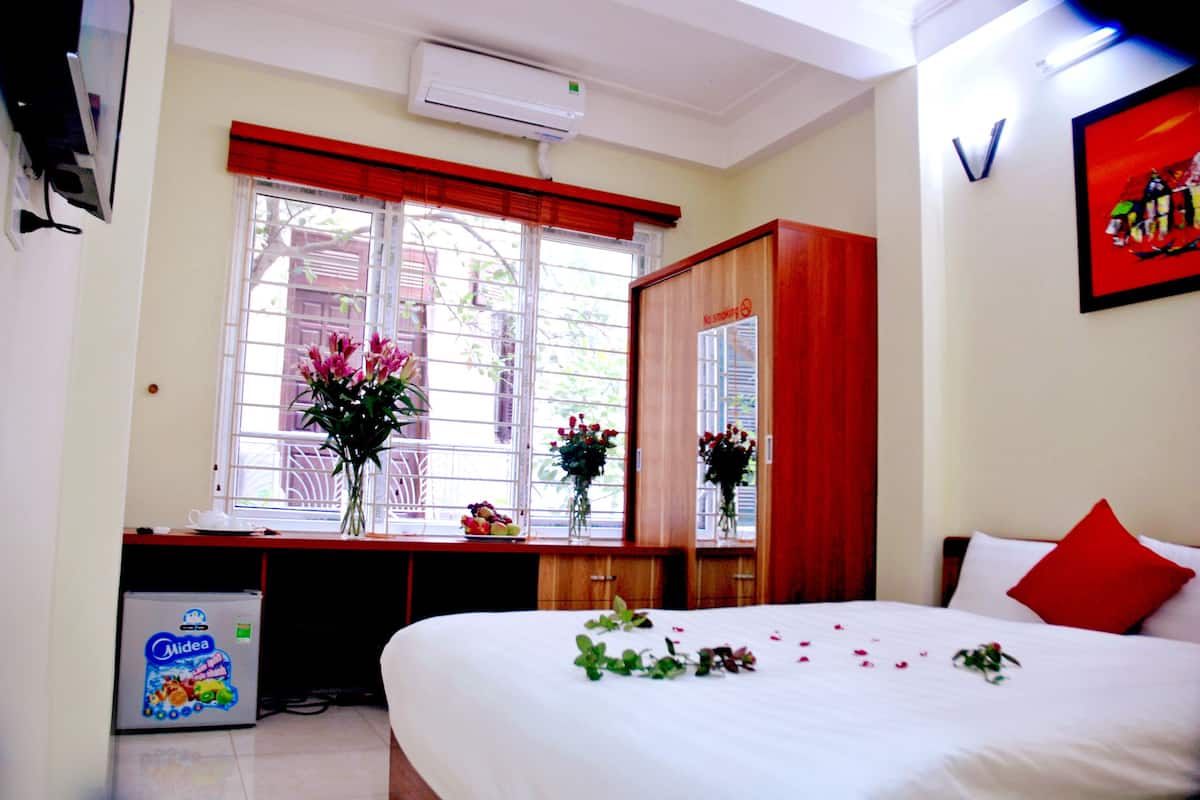A hotel room with a bed, a desk, a wardrobe, and a window with red curtains.