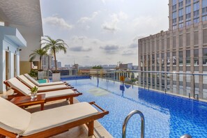 Una piscina en la azotea con sillones, una palmera y vistas panorámicas de la ciudad.