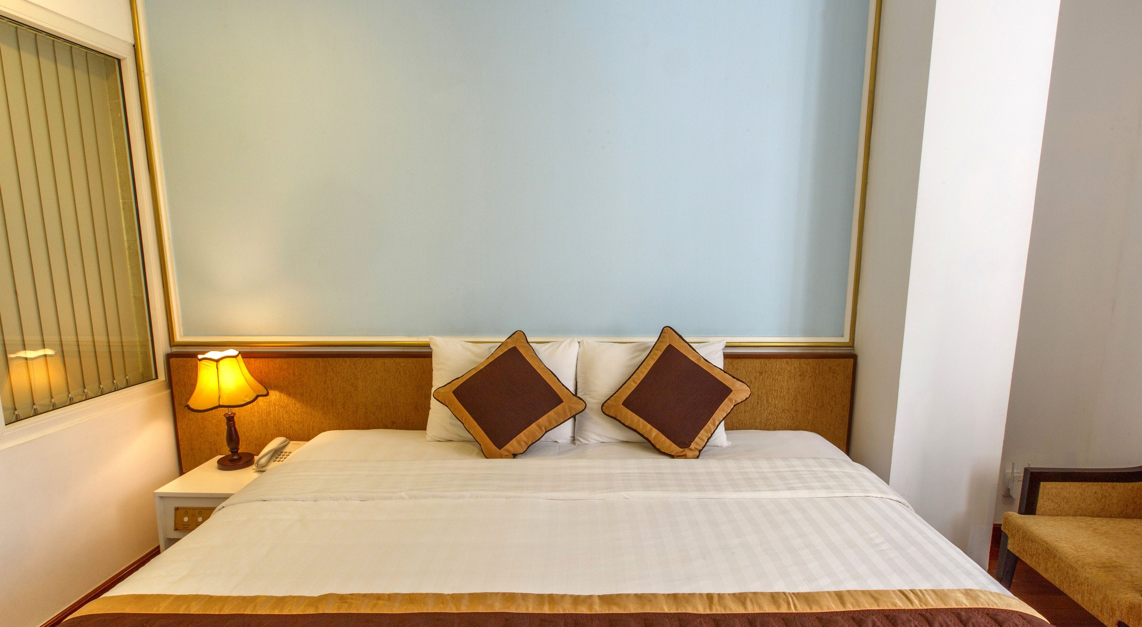 A hotel room with a large bed, two pillows, a bedside lamp, and a nightstand with a phone.
