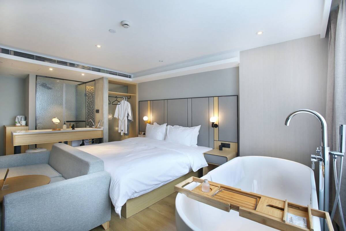 Een moderne hotelkamer met een groot bed, een aparte zithoek, een kaptafel met spiegel en een vrijstaand bad.