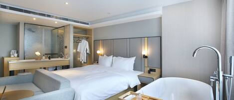 A modern hotel room with a large bed, a separate seating area, a vanity with a mirror, and a freestanding bathtub.