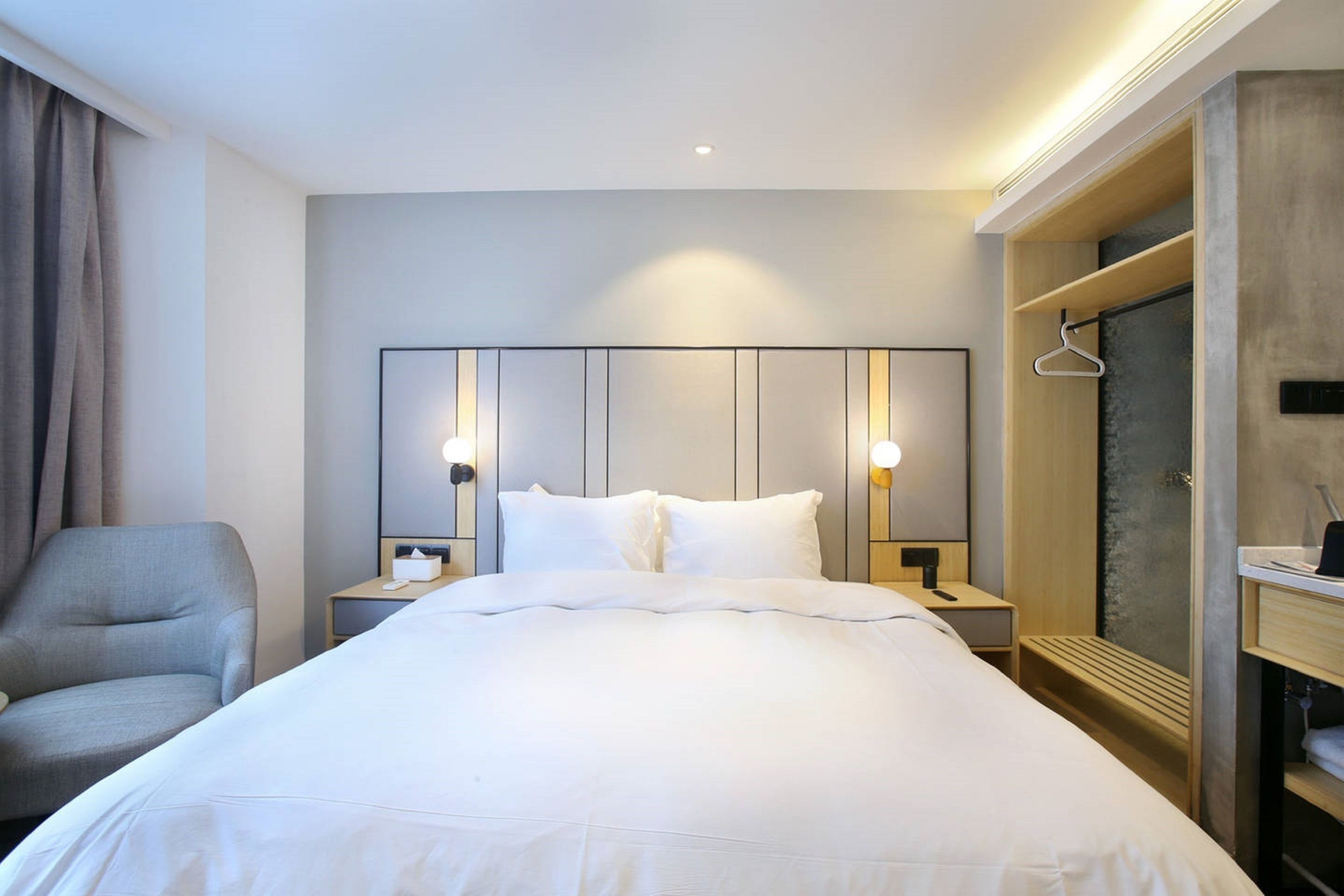 A hotel room with a large bed, a chair, bedside tables, and a wardrobe.