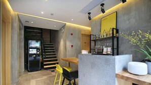 Un hall d’hôtel moderne comprenant un comptoir d’accueil, un escalier et un distributeur automatique.