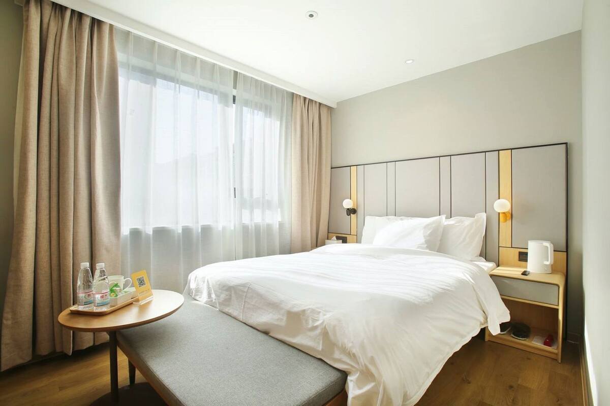 Een hotelkamer met een bed, nachtkastjes, een kleine tafel met stoel, en een raam met gordijnen.