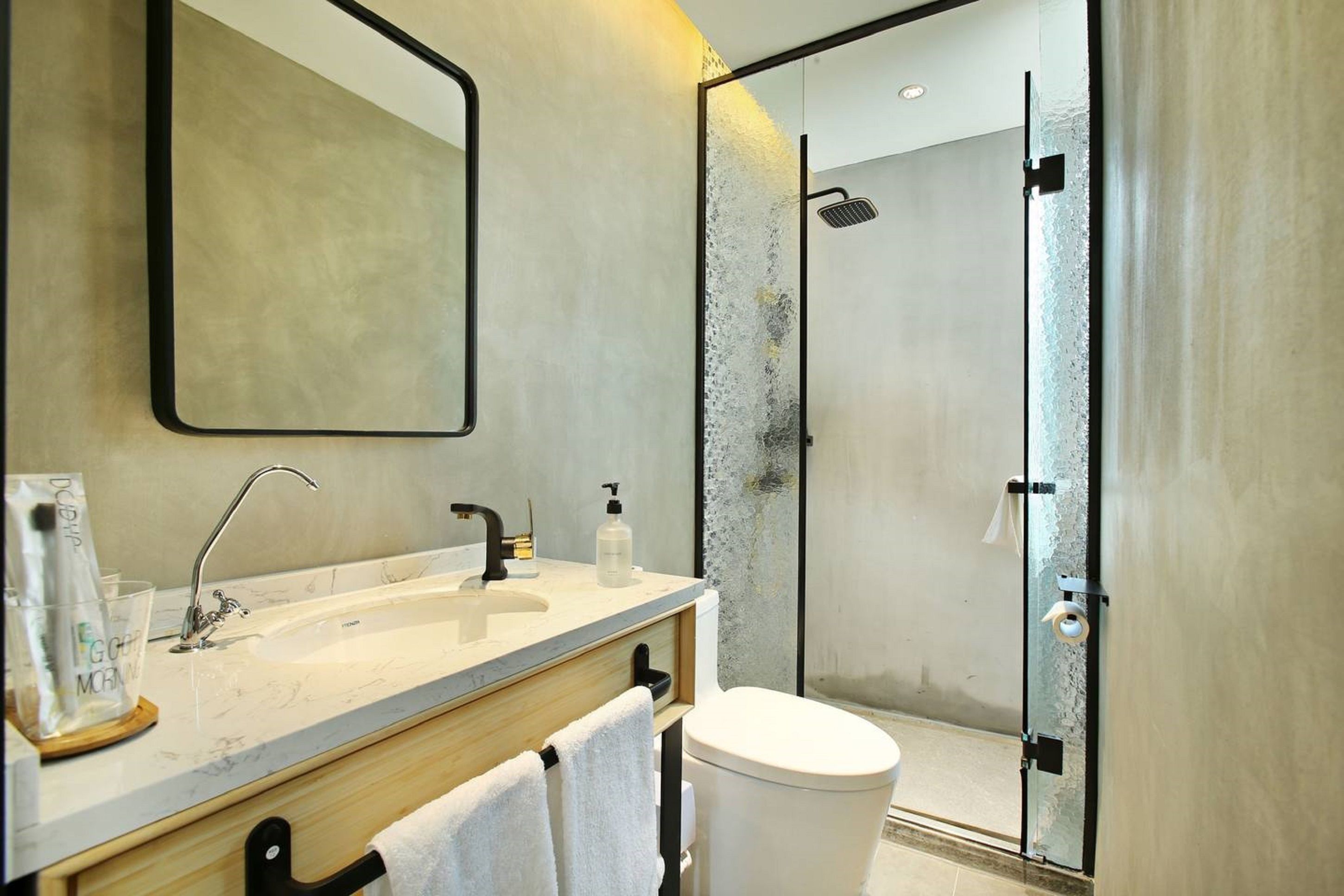 A modern bathroom with a large mirror, a sink with a faucet, a toilet, and a glass-enclosed shower area.