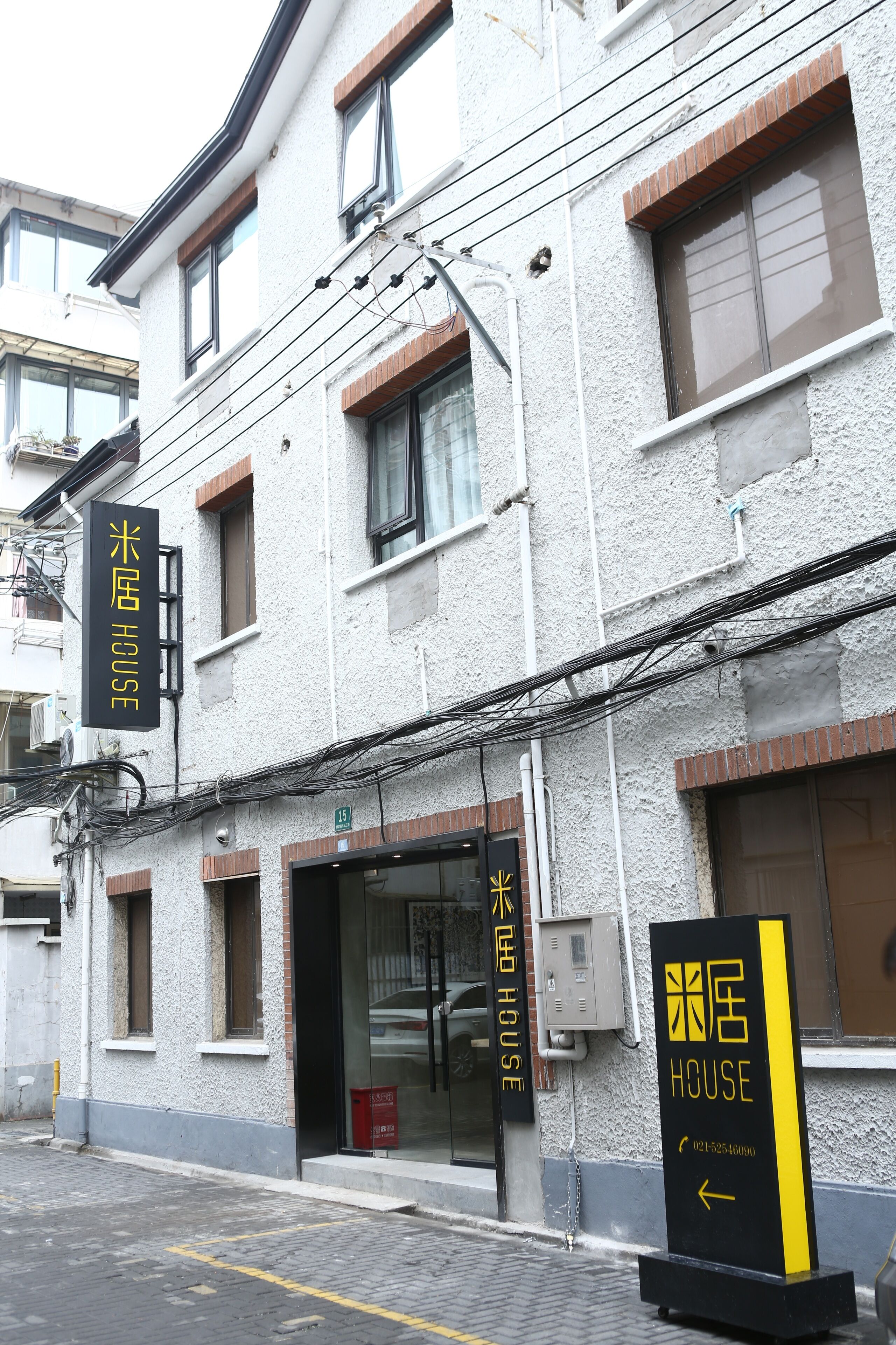 A building with a sign reading "HOUSE" and a smaller sign with Japanese characters. There are multiple windows and a door, with visible electrical wiring.