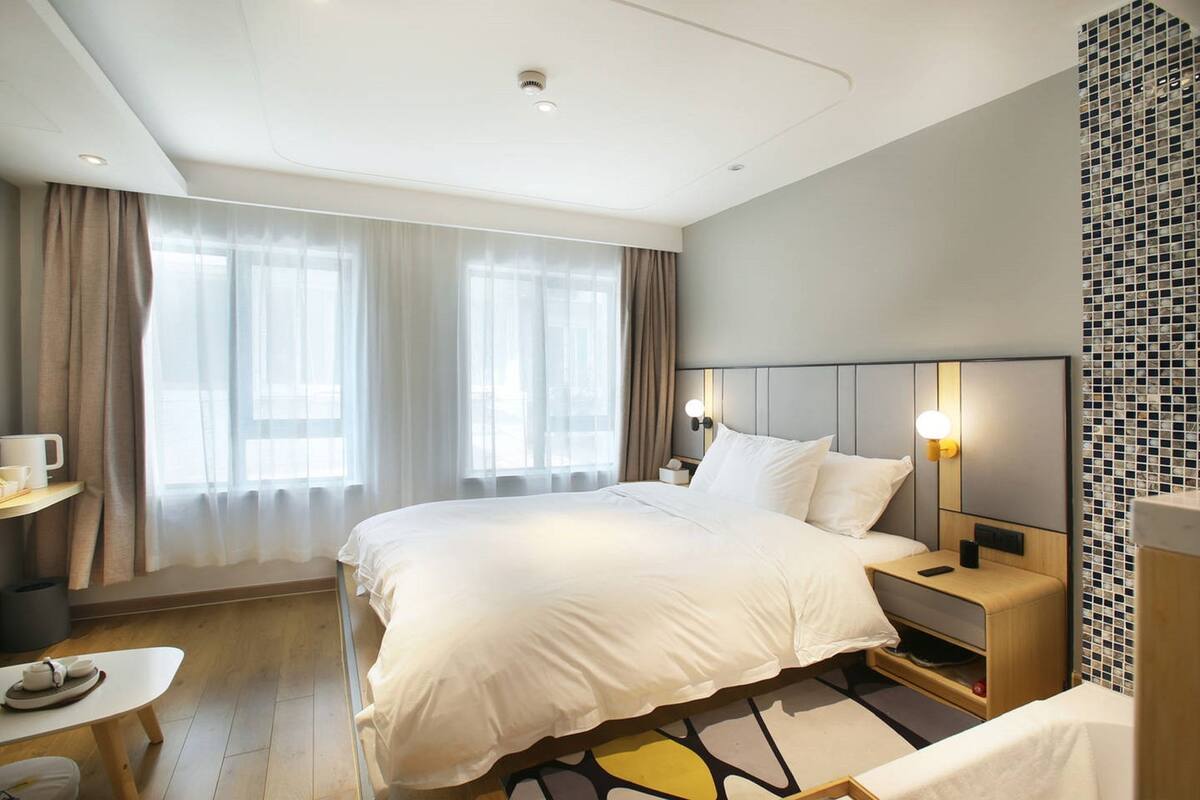 Een moderne hotelkamer met een groot bed, nachtkastjes, een klein bureau met een stoel, en een raam met gordijnen.
