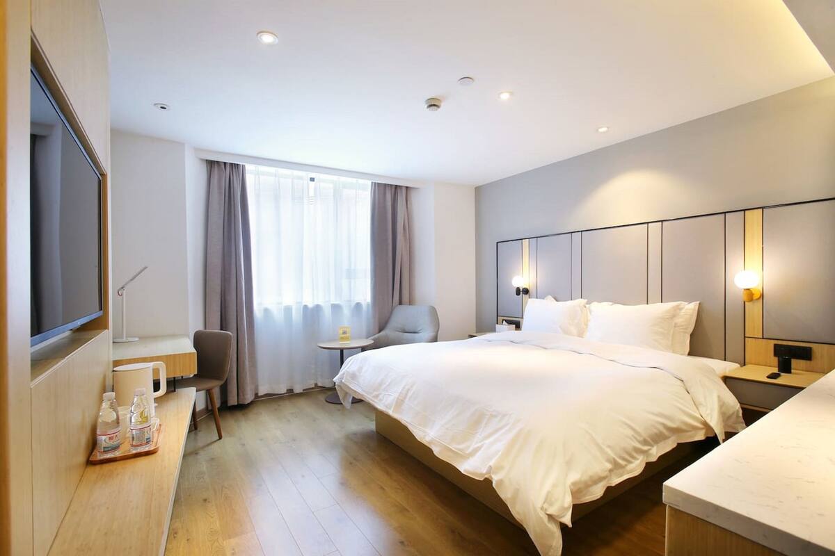 Een moderne hotelkamer met een groot bed, een bureau met stoel, een televisie en een raam met gordijnen.