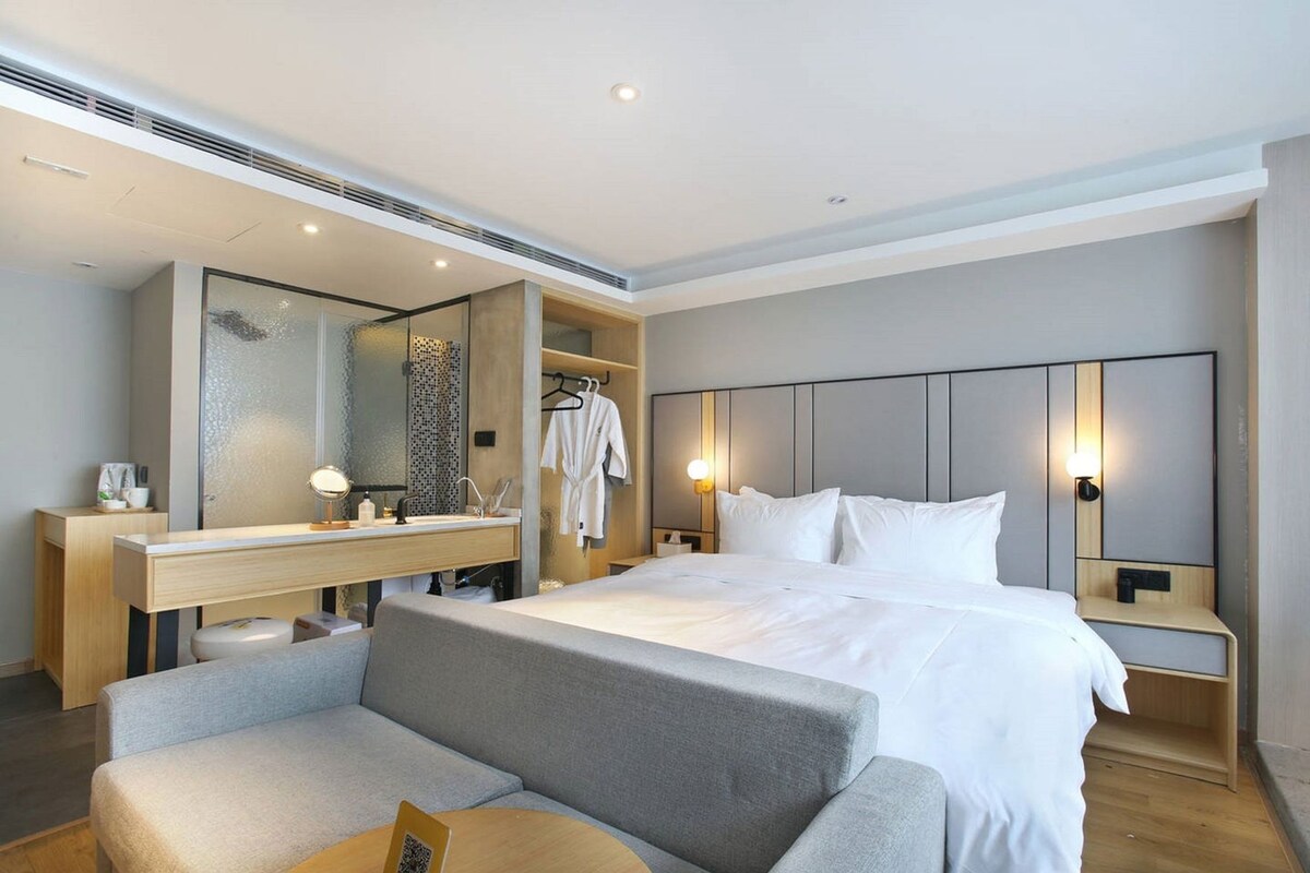 A modern hotel room with a large bed, a sofa, a vanity with a mirror, and two bedside lamps.