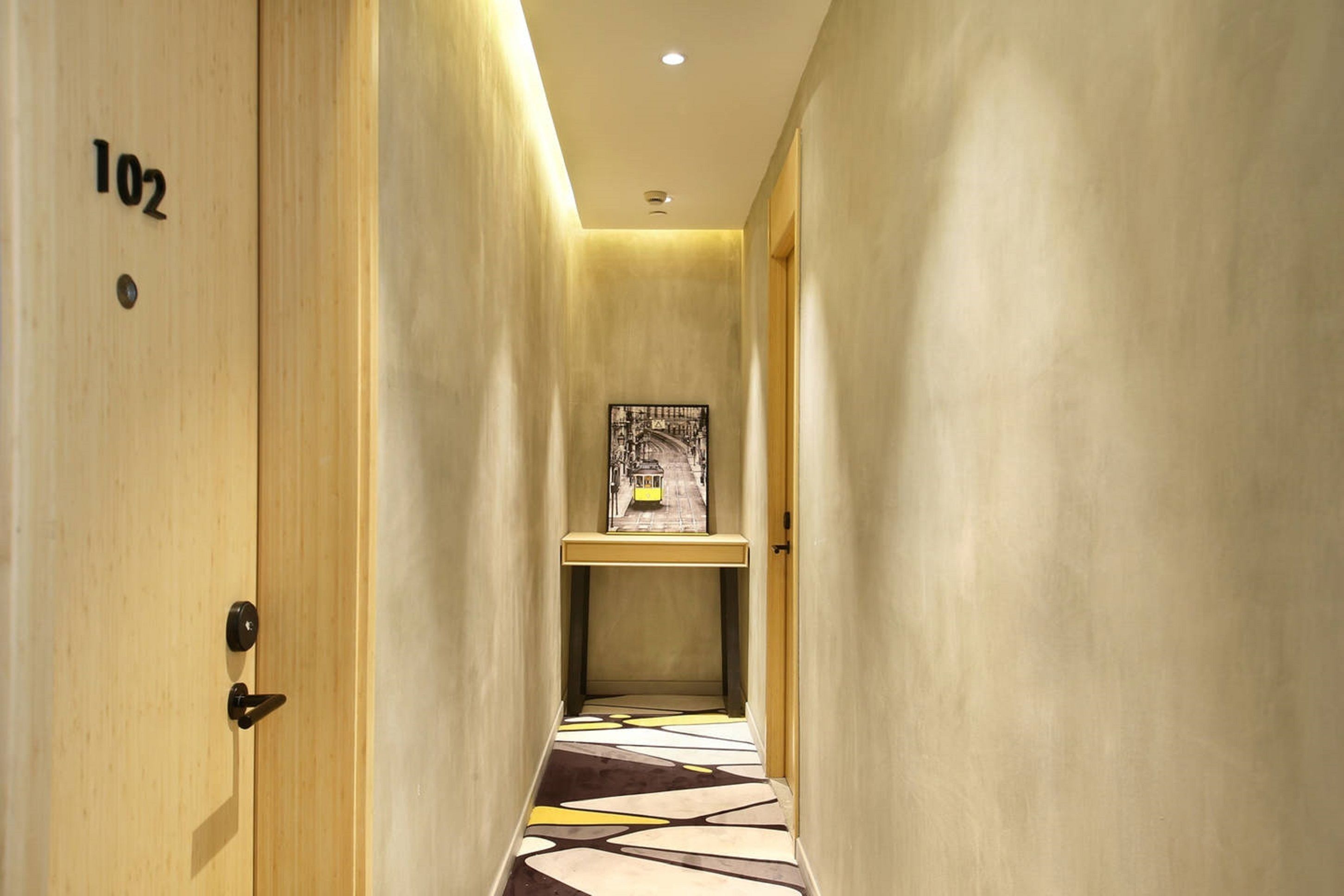 A narrow hallway with a wooden door labeled "102" and a small table with a framed picture.
