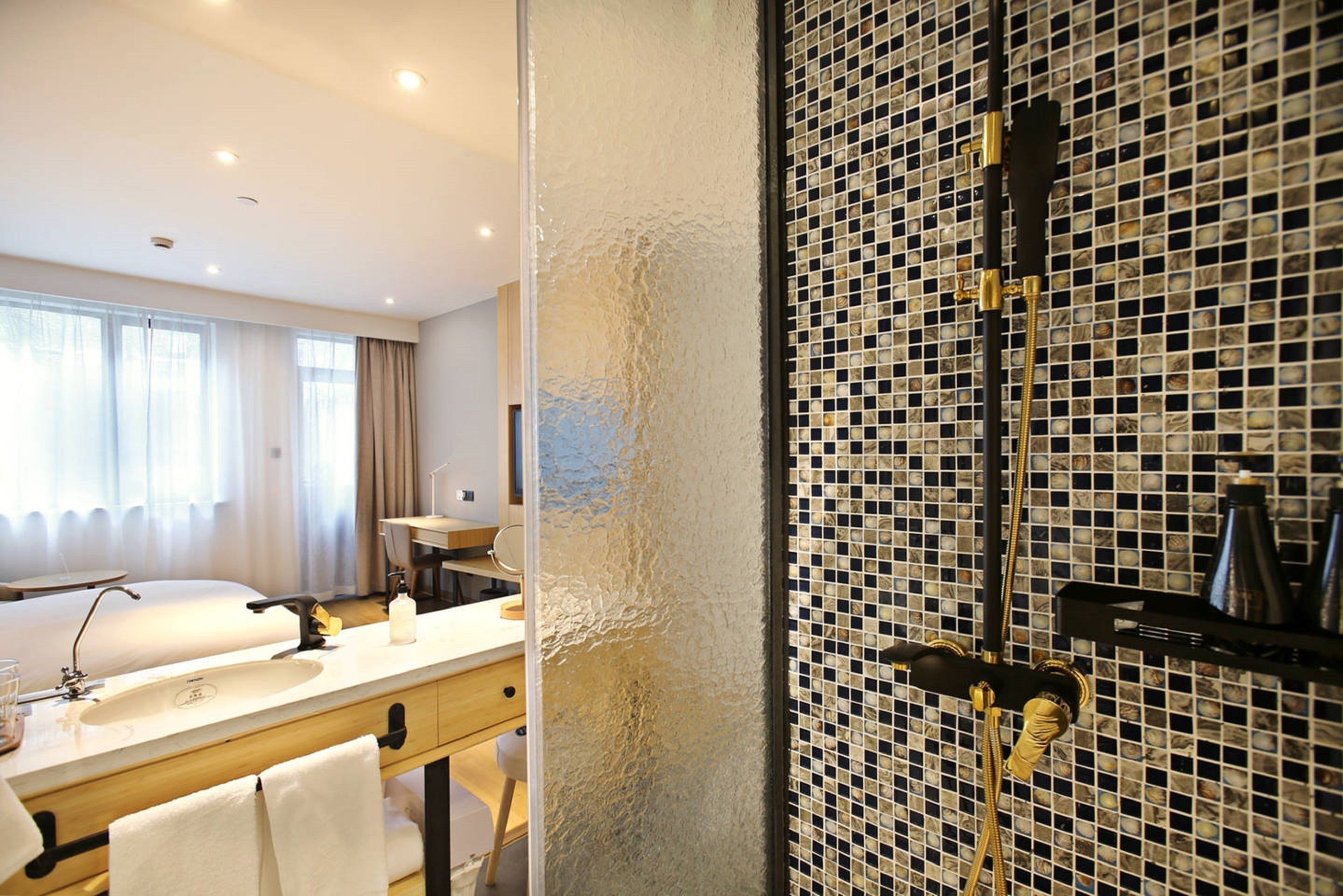 A hotel bathroom with a large mirror, a sink, and a shower area with a mosaic tile wall.