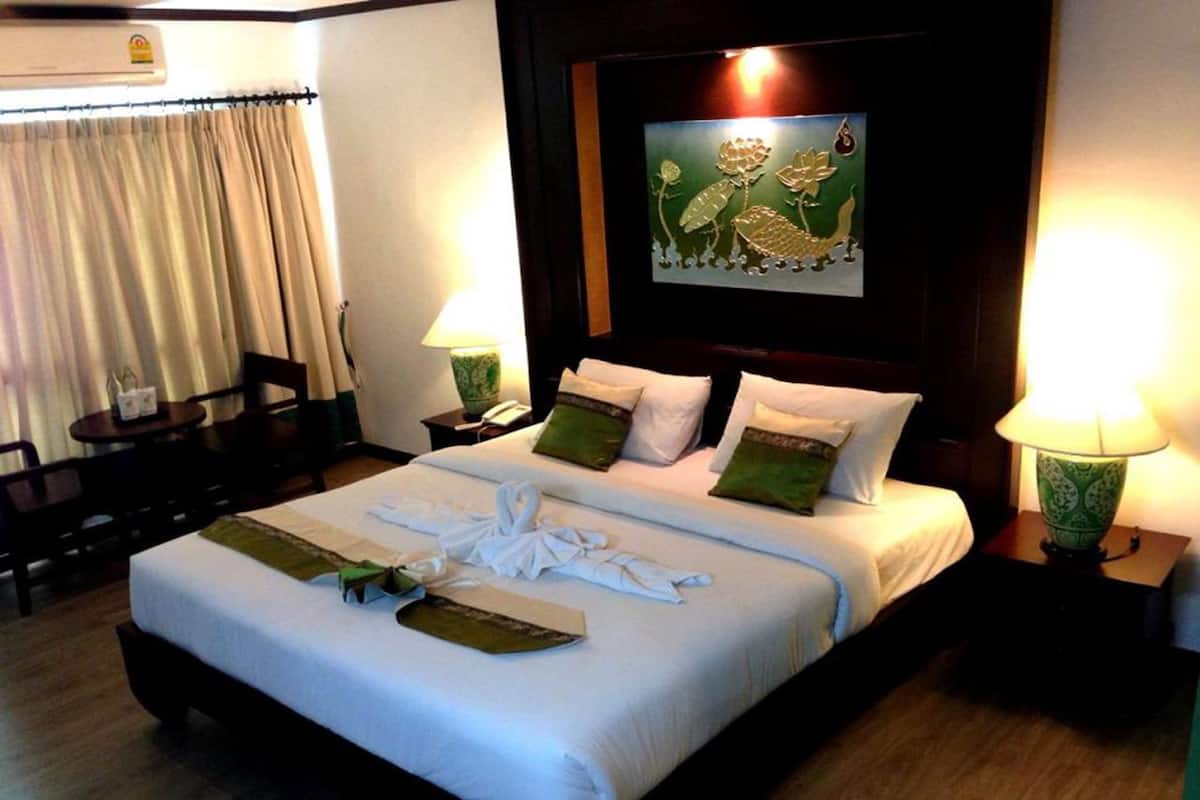 A hotel room with a neatly made bed, a painting on the wall, and two bedside lamps.