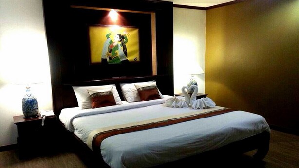 A hotel room with a large bed, two bedside tables with lamps, a framed picture on the wall, and a wooden headboard. - Chour Palace Hotel (Mae Sai)