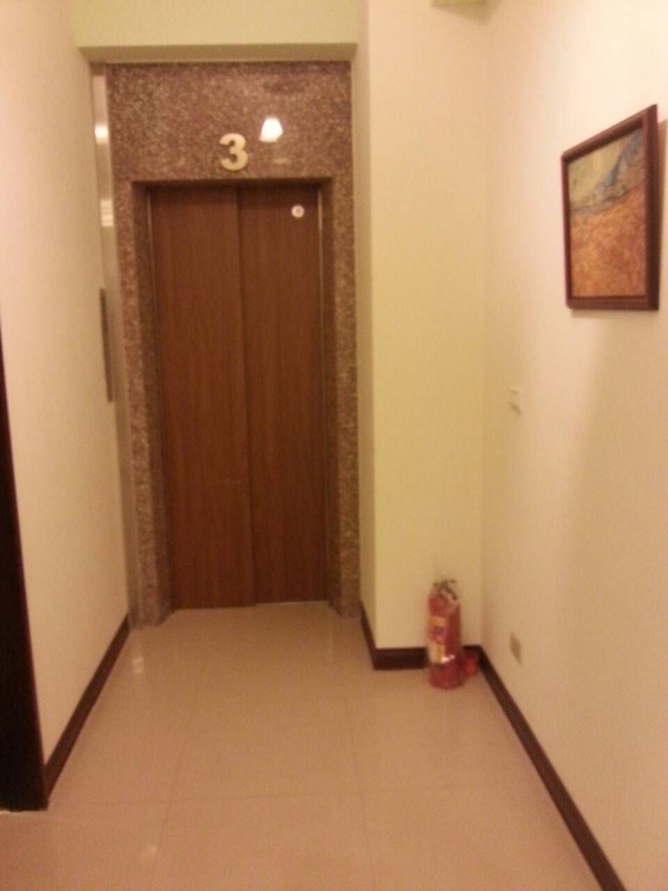 A hallway with a wooden door marked with the number 3, a fire extinguisher, and a framed picture on the wall.